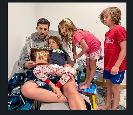 A father reads There's a Snake Down There to his three children on the couch
